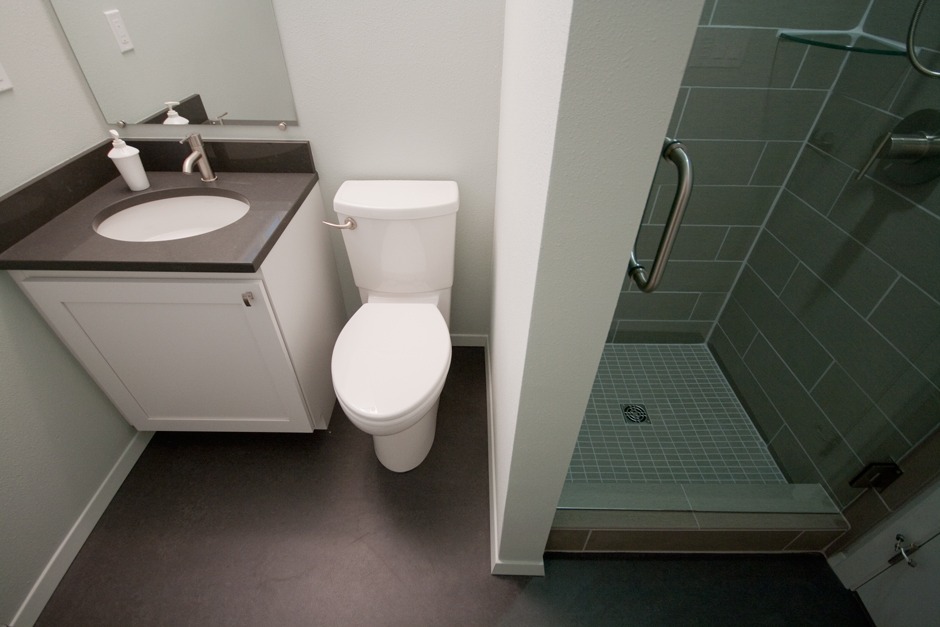 New bathroom with tiled shower stall and dark gray quartz counter.