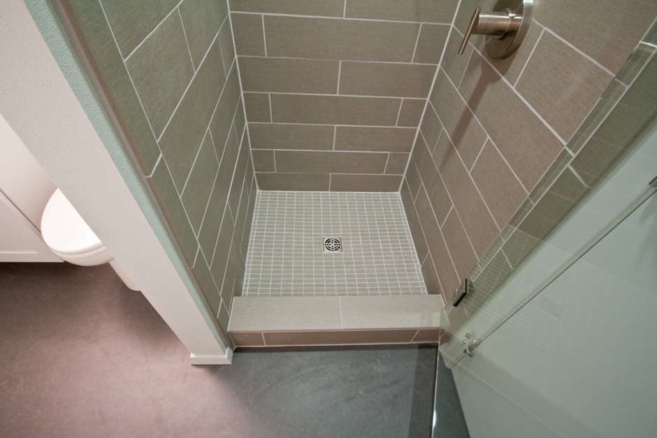 Gray tile shower pan with square drain and custom bullnosed curb top.