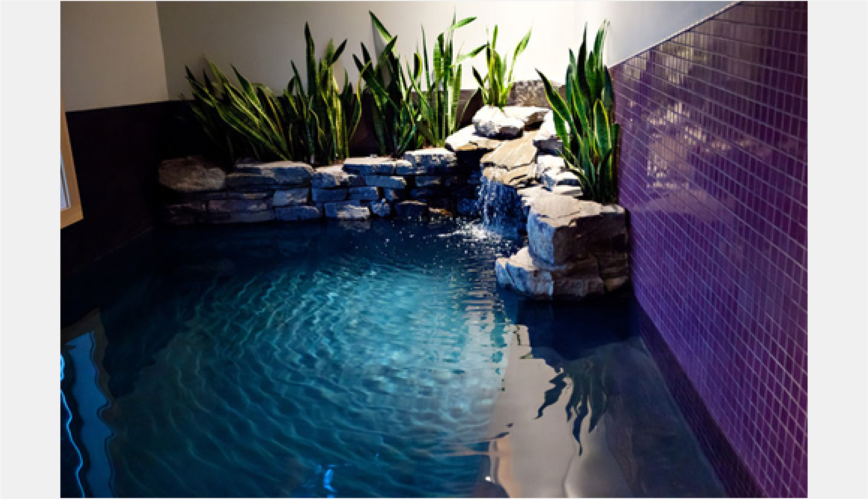 waterfall in indoor swimming pool with bench and live plants