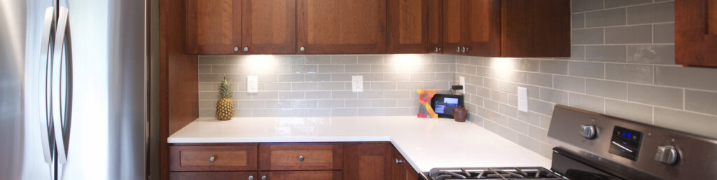 kitchen with green subway tile backsplash and white quartz counters with red cherry cabinets