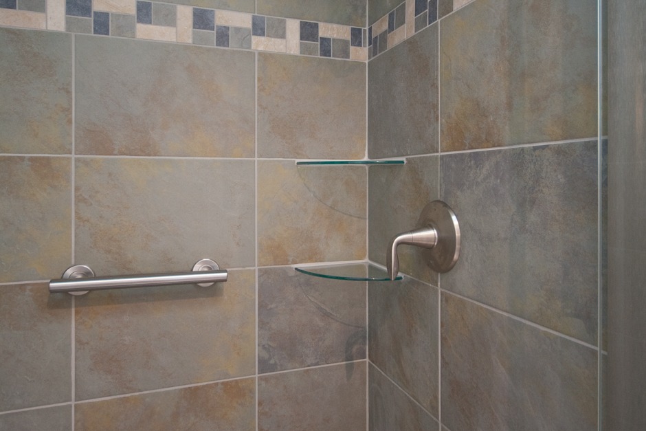 close up of tiled shower surround with glass corner shelves and horizontal grab bar