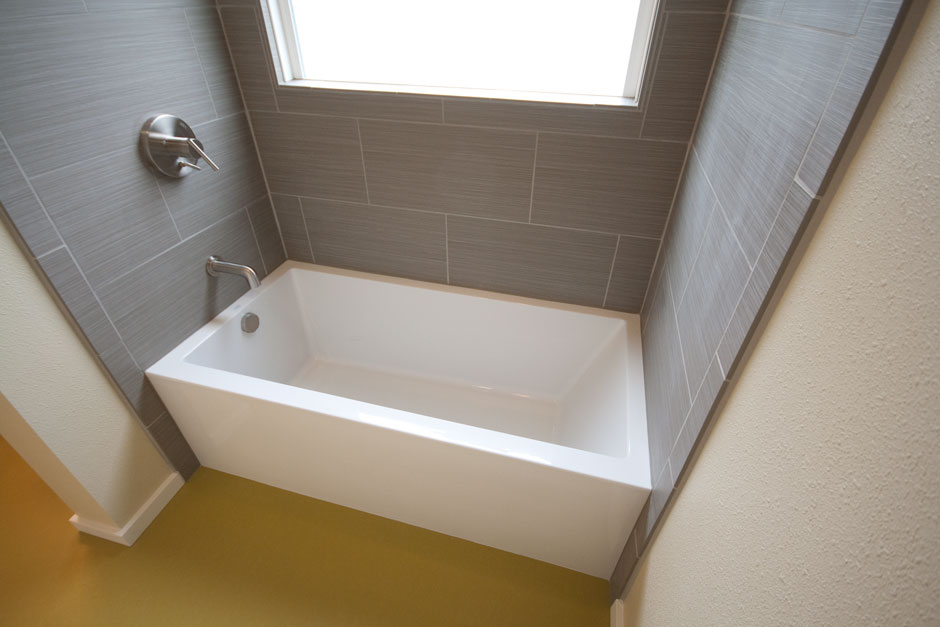 Laundry and bathroom remodel; flat-front tub with gray tile surround and large window shown.