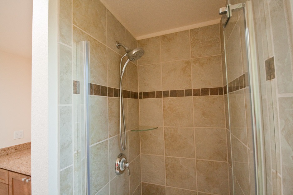 New shower installation with dark brown tile accent band, sandy beige field tile, glass shelf.
