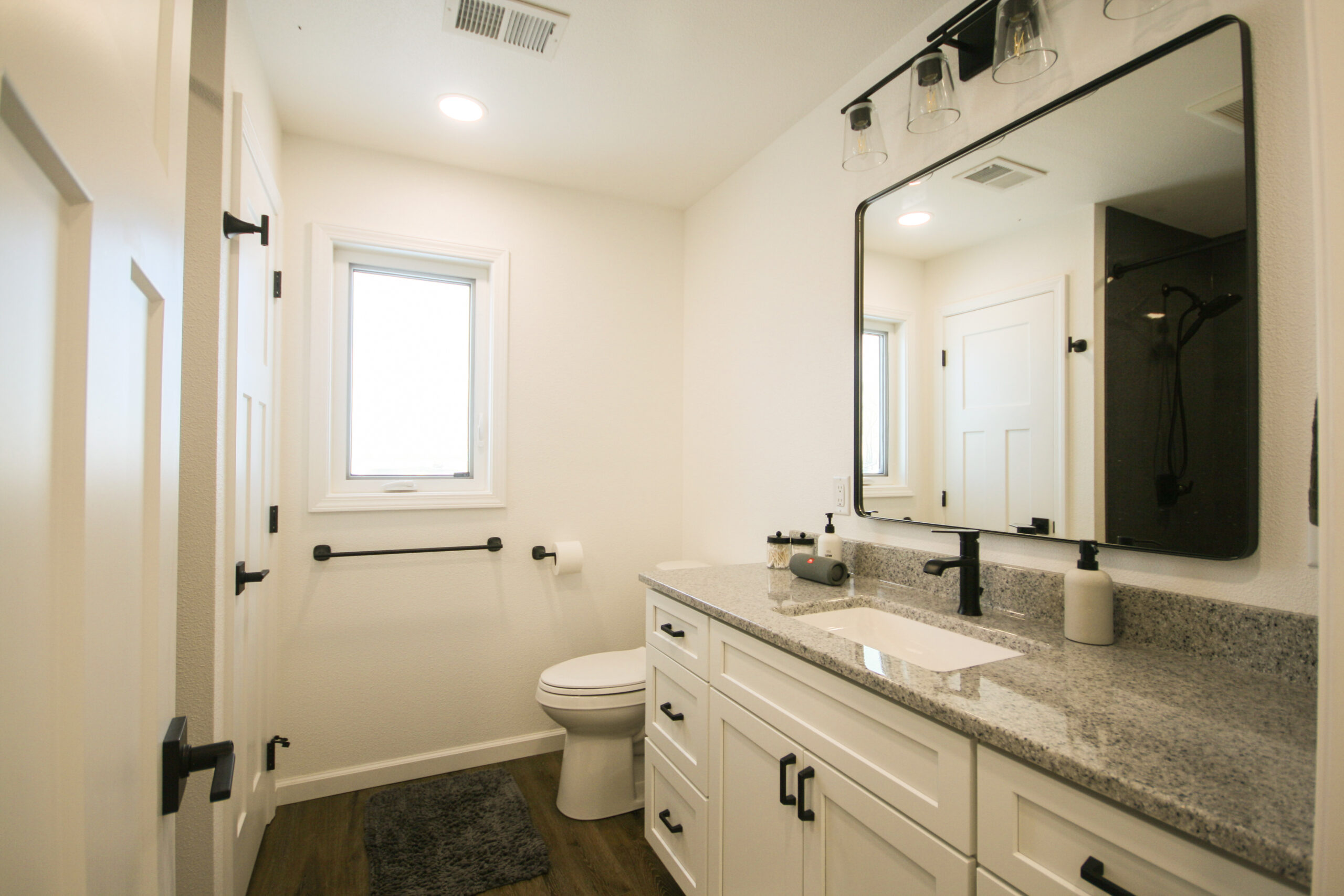 Bathroom Builder bathroom pictures: Bathroom remodel with gray vanity counter, black-framed mirror and brown vinyl plank flooring